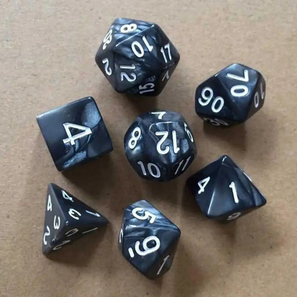 A collection of black acrylic polyhedral dice, including d10s and d6s, scattered on a brown surface.