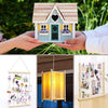 A wooden house craft kit featuring a light blue facade, green door, and white trim, held by hands.