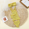 A yellow knitted doll outfit set for a baby, including a top, shorts, and a bow, displayed on a woven mat.
