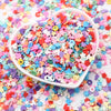A heart-shaped bowl filled with colorful polymer clay sprinkles for slime and craft decor scattered on a white surface.