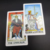 Two tarot cards, The Emperor and Queen of Swords, are displayed against a dark background.