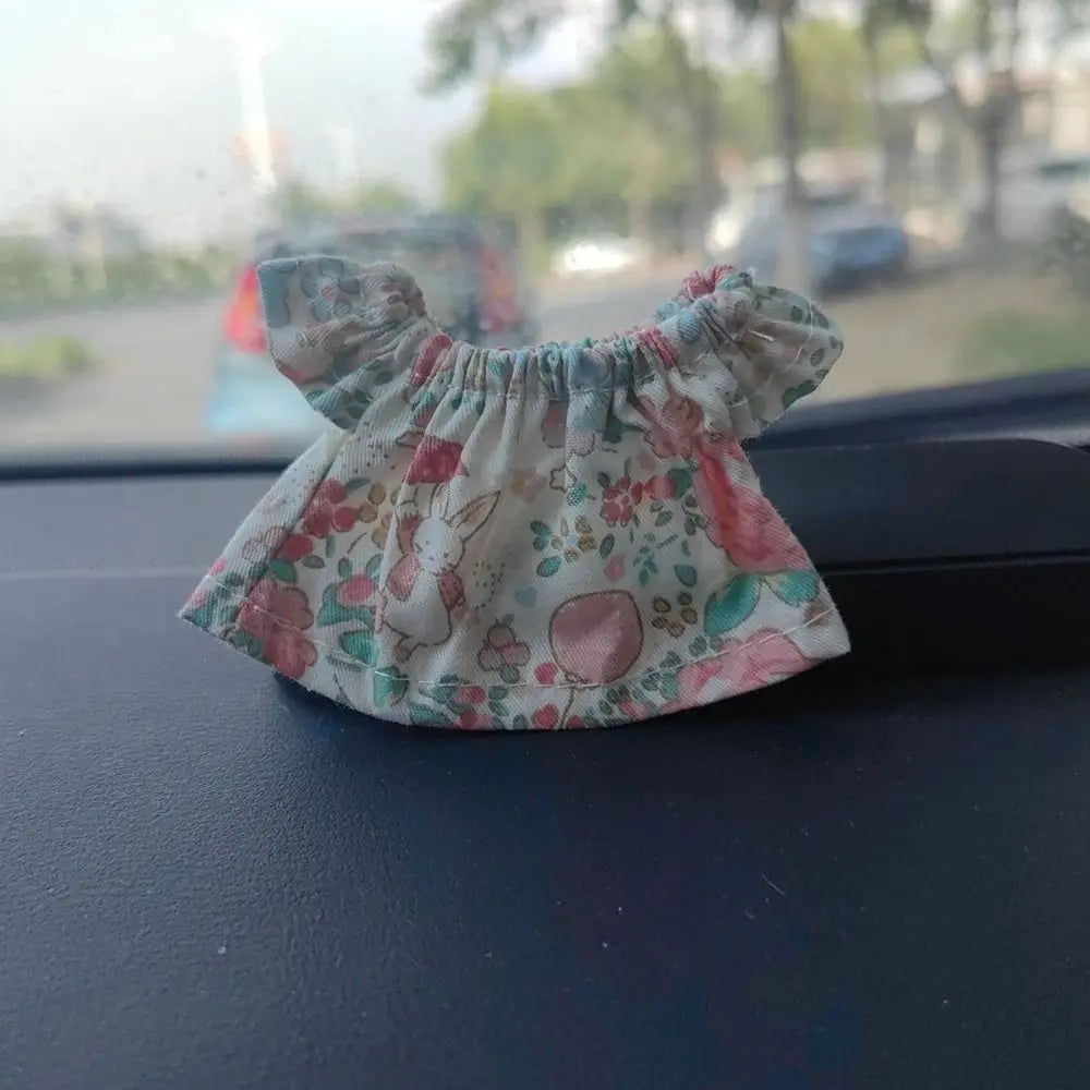 A light pink and green floral fabric garment with ruffled trim, likely clothing for a fashion doll.