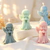 Three silicone praying angel molds in mint green, pale blue, and pink are displayed on a white surface with lit candles.