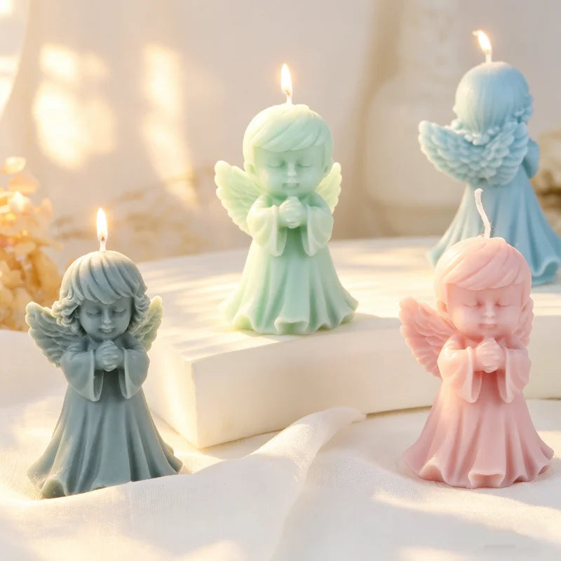 Three silicone praying angel molds in mint green, pale blue, and pink are displayed on a white surface with lit candles.