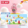 A pink Care Bear figurine stands in a cloud setting with colorful bears and rainbow elements.