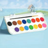 A portable watercolor paint set with various colored paints and a brush displayed outdoors against a scenic background.