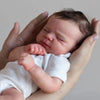 A newborn baby doll with hand-rooted hair is being held by a person.