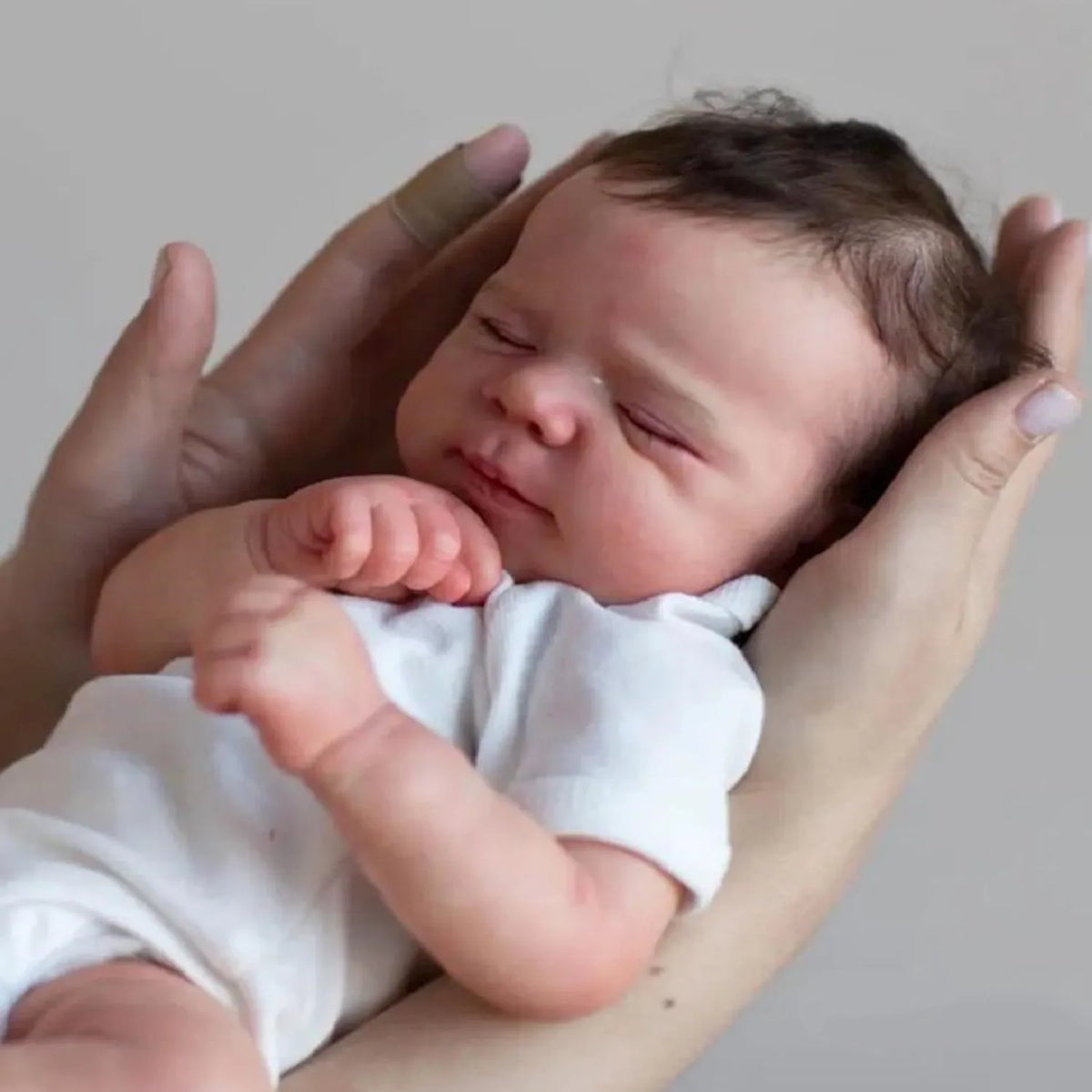 A newborn baby doll with hand-rooted hair is being held by a person.
