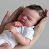 A newborn baby doll with hand-rooted hair is being held by a person's hands.