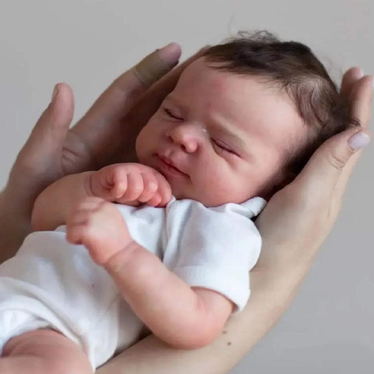 A newborn baby doll with hand-rooted hair is being held by a person's hands.