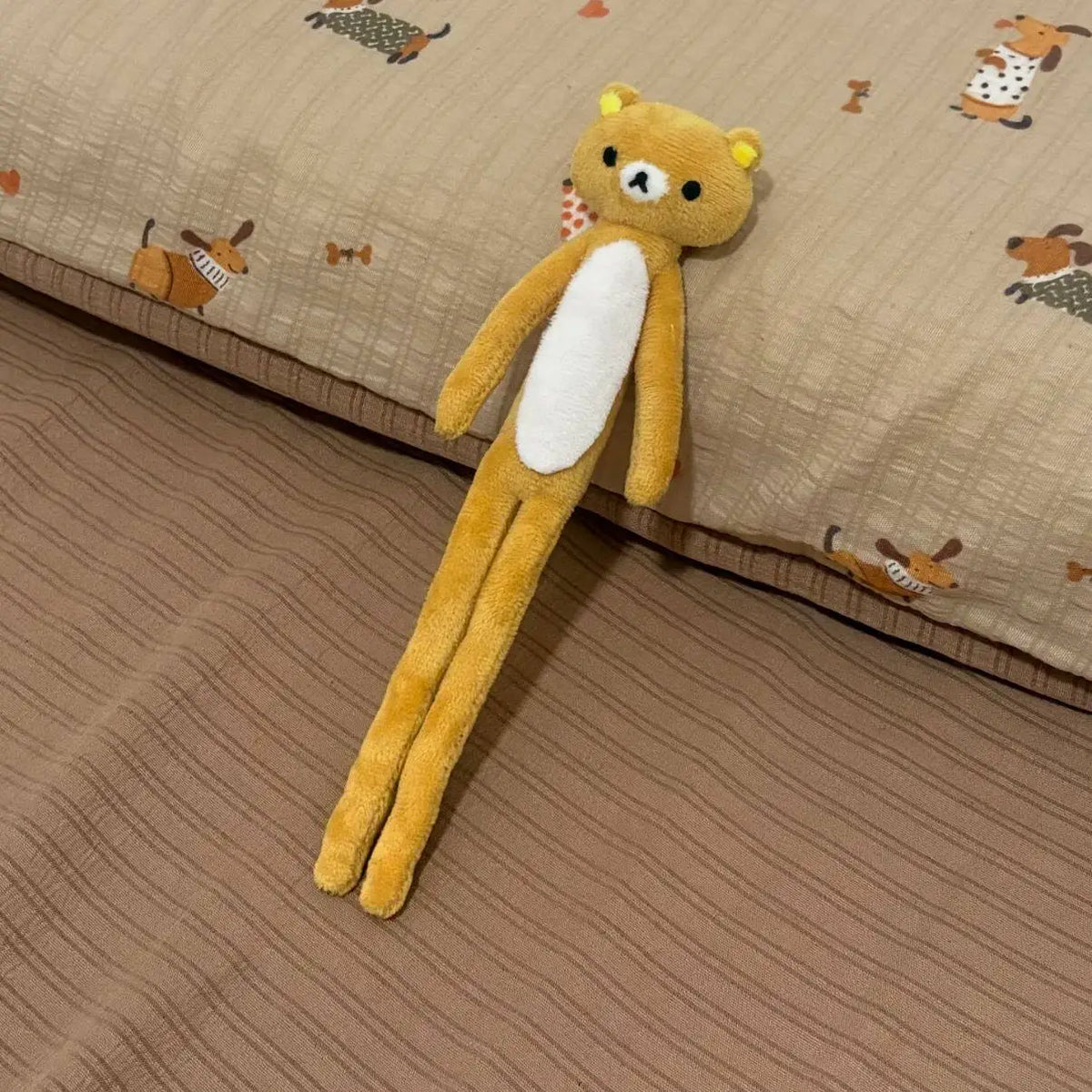 A yellow and white stuffed bear plushie lying on a beige fabric surface.