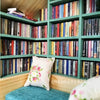 A wooden bookshelf filled with miniature books and decorated with a pink floral pillow.