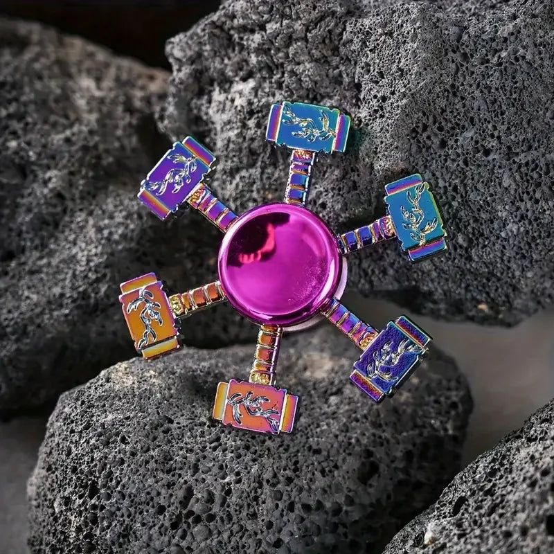 A colorful metal fidget spinner with purple, blue, and orange accents resting on dark gray rocks.