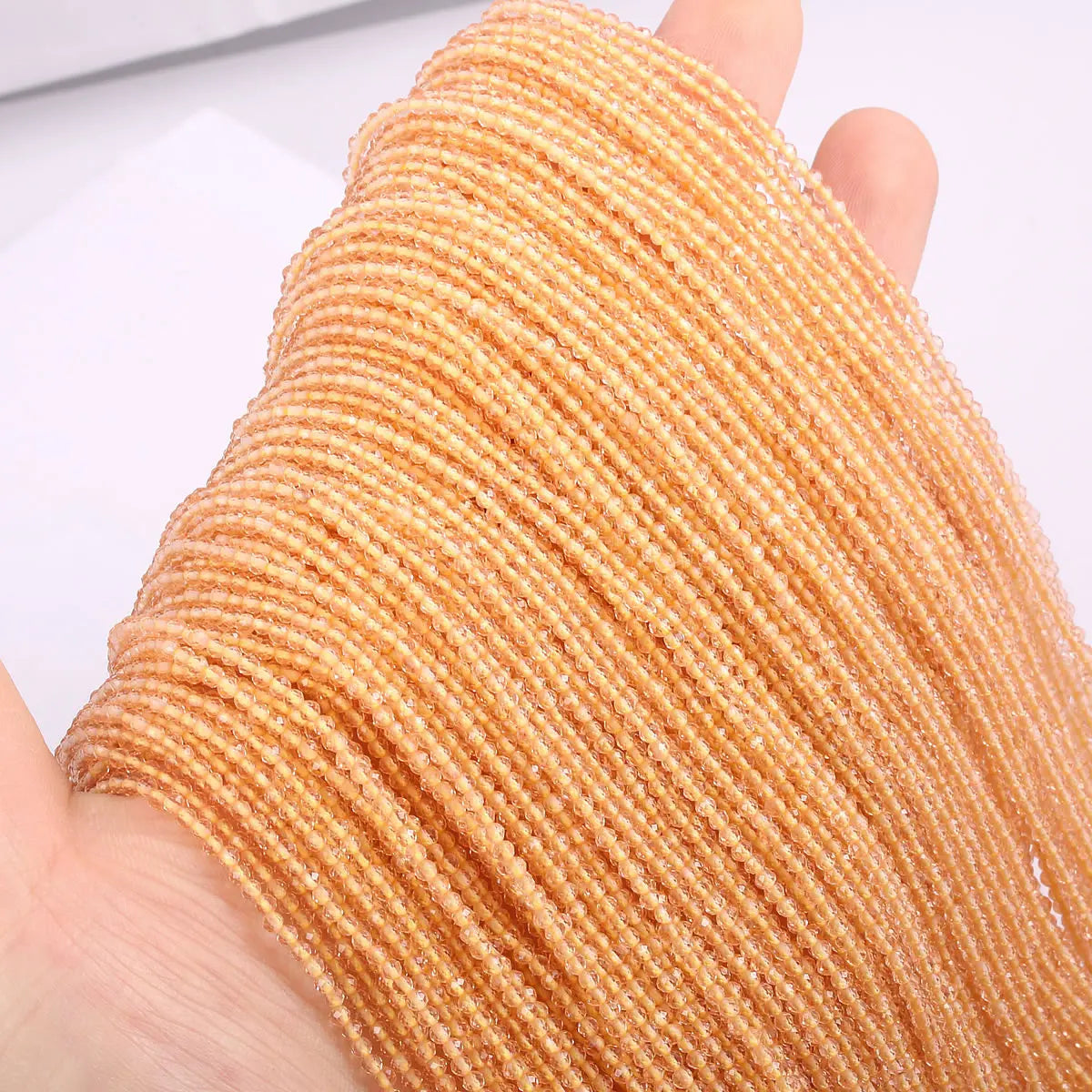 A hand holds a strand of faceted natural stone beads in a warm golden-orange color.