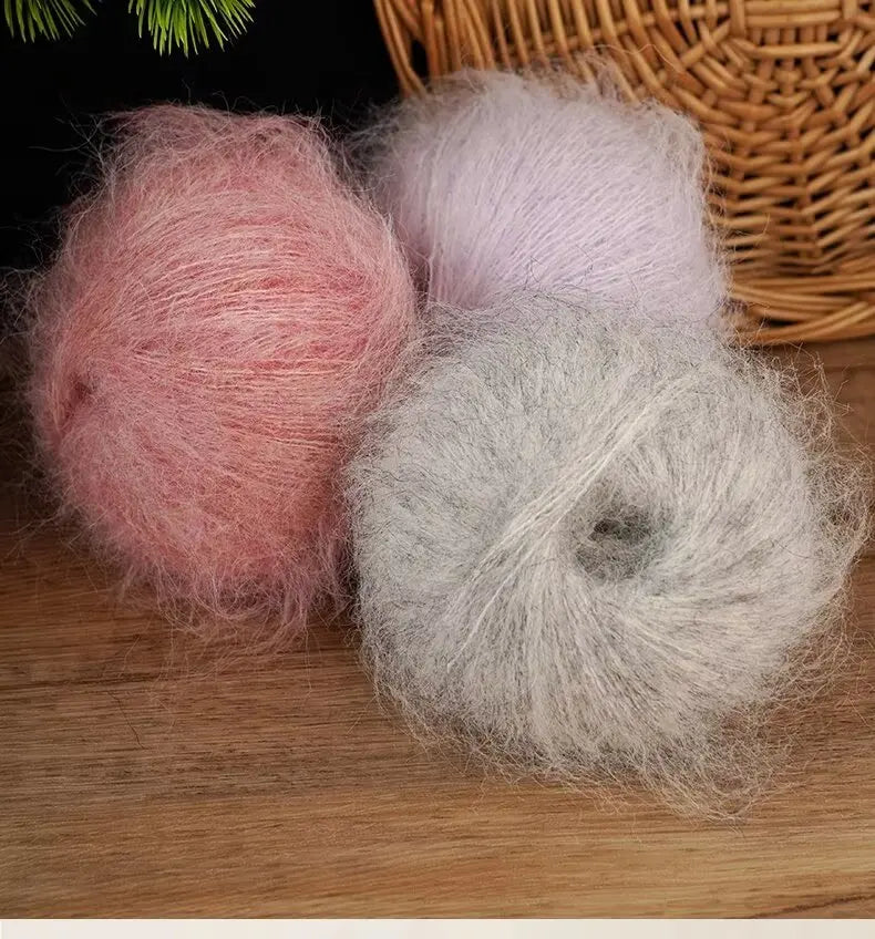 Three balls of long-haired alpaca blend yarn in shades of pink, lavender, and gray resting on a wooden surface.