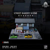 A 1:64 scale diorama depicting a street bakery scene with several diecast cars.
