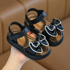 A pair of black and white bow detail breathable summer sandals being held by a hand.