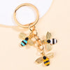 Gold-toned bee and daisy enamel flower keychain with a circular split ring.
