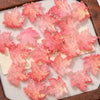 Pink maple leaf glass beads scattered on a light surface.