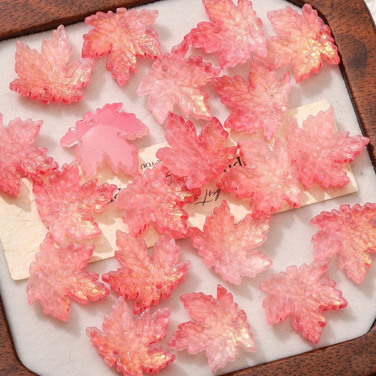 Pink maple leaf glass beads scattered on a light surface.