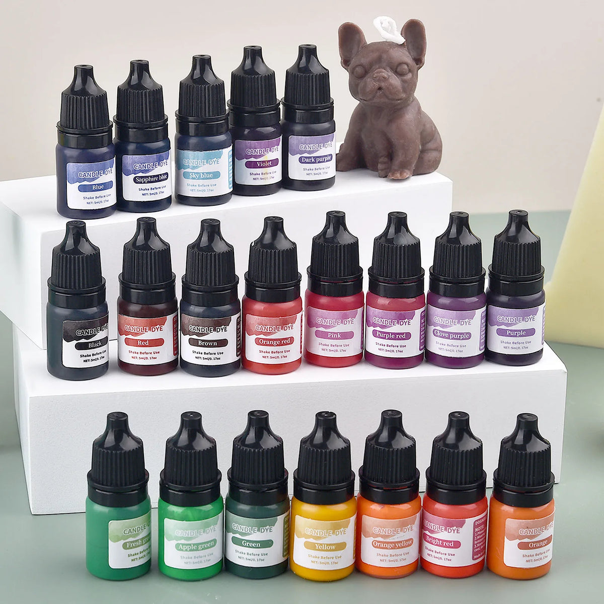 A collection of dark brown and purple liquid candle and soap colorants in glass bottles next to a small dog figurine.