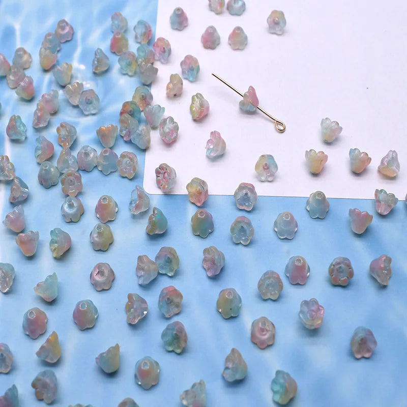 A collection of colorful glass beads shaped like lily of the valley flowers scattered on a white and blue surface.