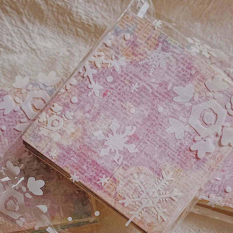 A sheet of textured pink paper decorated with white snowflakes and floral elements for junk journals