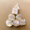 A stack of seven glitter gold polyhedral dice showing various numbers and angles on a brown surface.