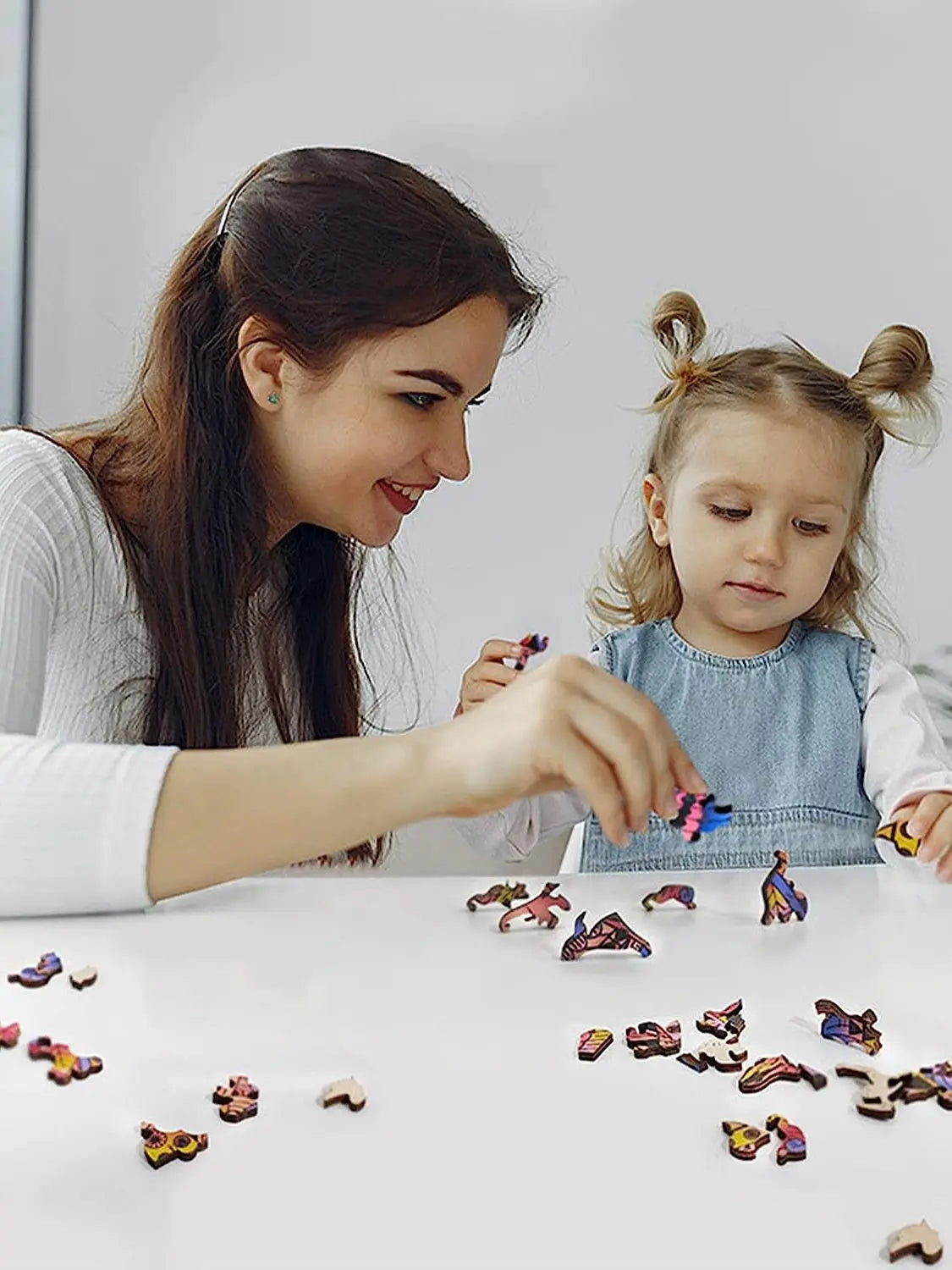 A woman is helping a young girl assemble a wooden jigsaw puzzle featuring various animal shapes.