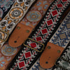 Close-up of an embroidered guitar strap featuring geometric patterns on fabric with brown leather ends.