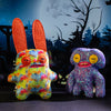 A colorful monster plush doll with orange ears sitting in front of a dark, spooky background.
