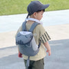 Un jeune garçon portant une casquette de baseball grise et un sac à dos anti-perte gris avec une sangle de sécurité blanche.