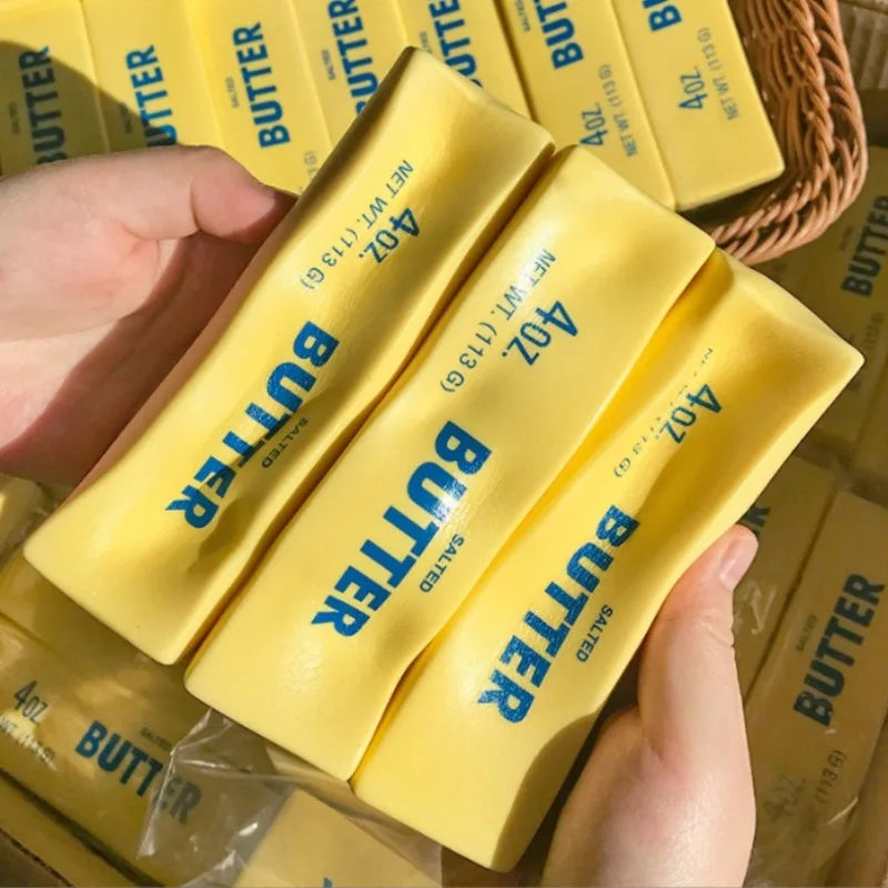 Eine Hand hält ein gelbes Butter-Pressspielzeugprodukt in klarem Plastik verpackt.