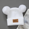 White knit baby beanie hat with fluffy bear ears and a brown mini tag