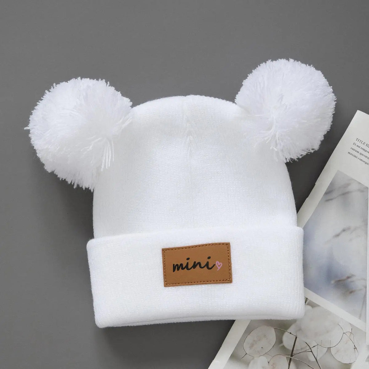 White knit baby beanie hat with fluffy bear ears and a brown mini tag