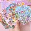 A hand is holding a colorful set of cartoon mini town diorama stickers featuring various buildings and characters.