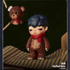 A collectible figurine of a dark-haired character wearing a red scarf and brown clothing, with a small teddy bear accessory a