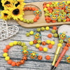 A collection of colorful 3D bee silicone beads and craft supplies arranged on a wooden board.