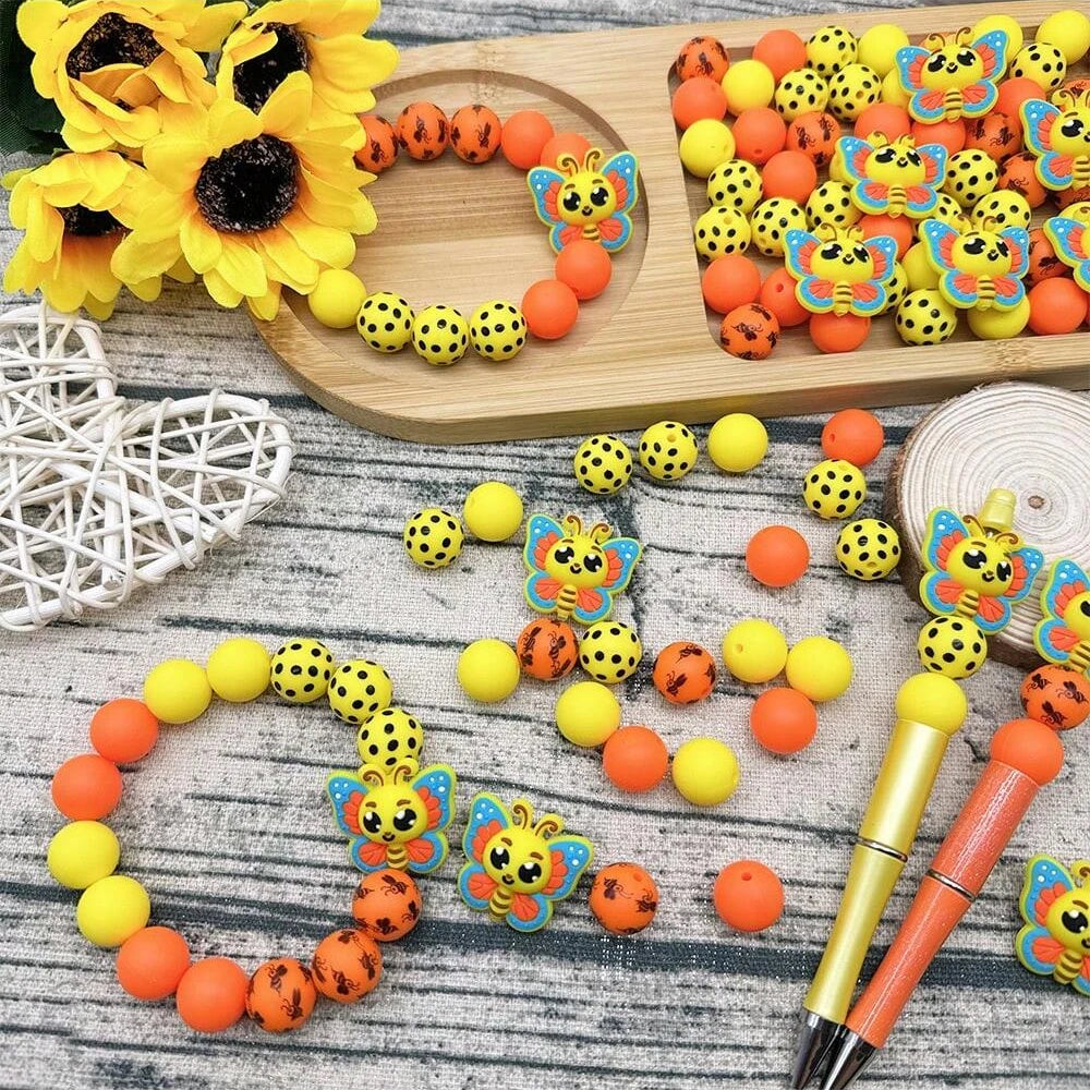 A collection of colorful 3D bee silicone beads and craft supplies arranged on a wooden board.