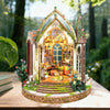 A detailed diorama of a wooden floral book nook kit featuring an arched window and miniature landscape.