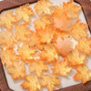 A collection of translucent orange maple leaf glass beads arranged on a wooden tray.