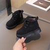A pair of black kids' winter leather boots with a brown cuff resting on a gray surface.