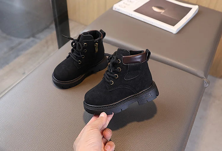A pair of black kids' winter leather boots with a brown cuff resting on a gray surface.