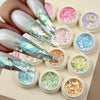 A collection of iridescent opal and mermaid chrome nail glitter pigments in small pots arranged on a light background.