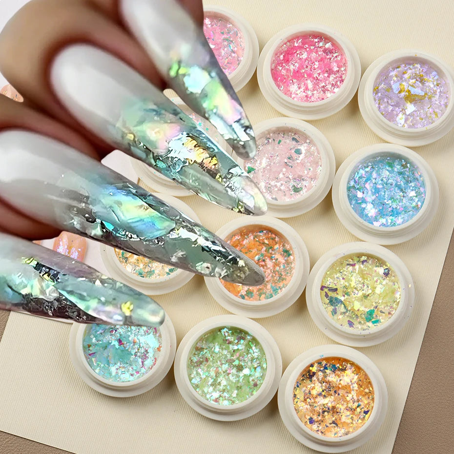 A collection of iridescent opal and mermaid chrome nail glitter pigments in small pots arranged on a light background.