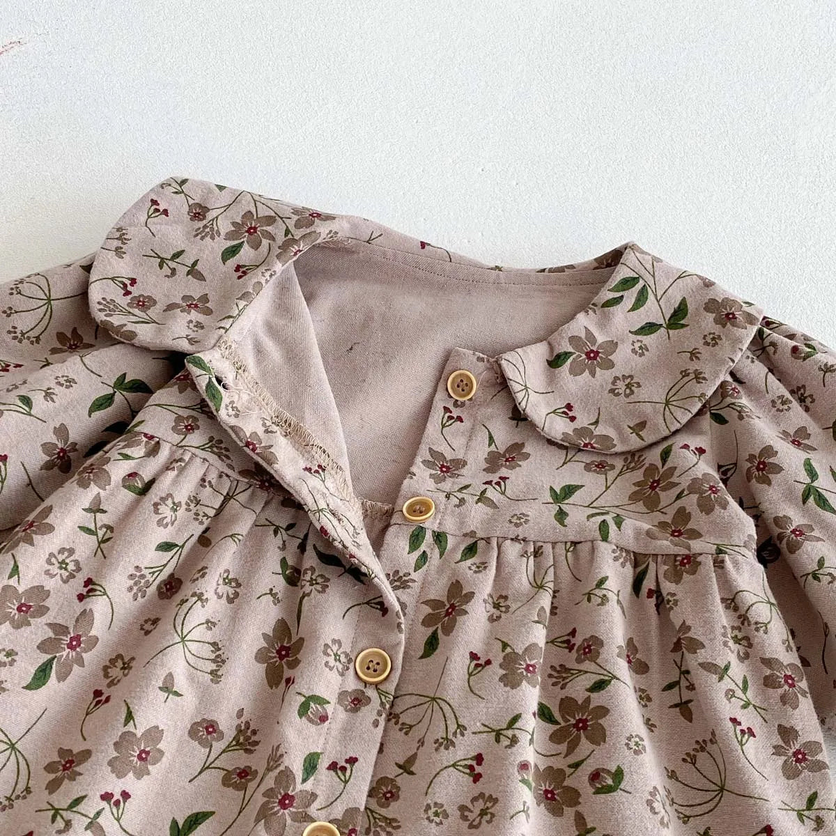 A light pink floral print baby girl jumpsuit with a doll collar and long sleeves.