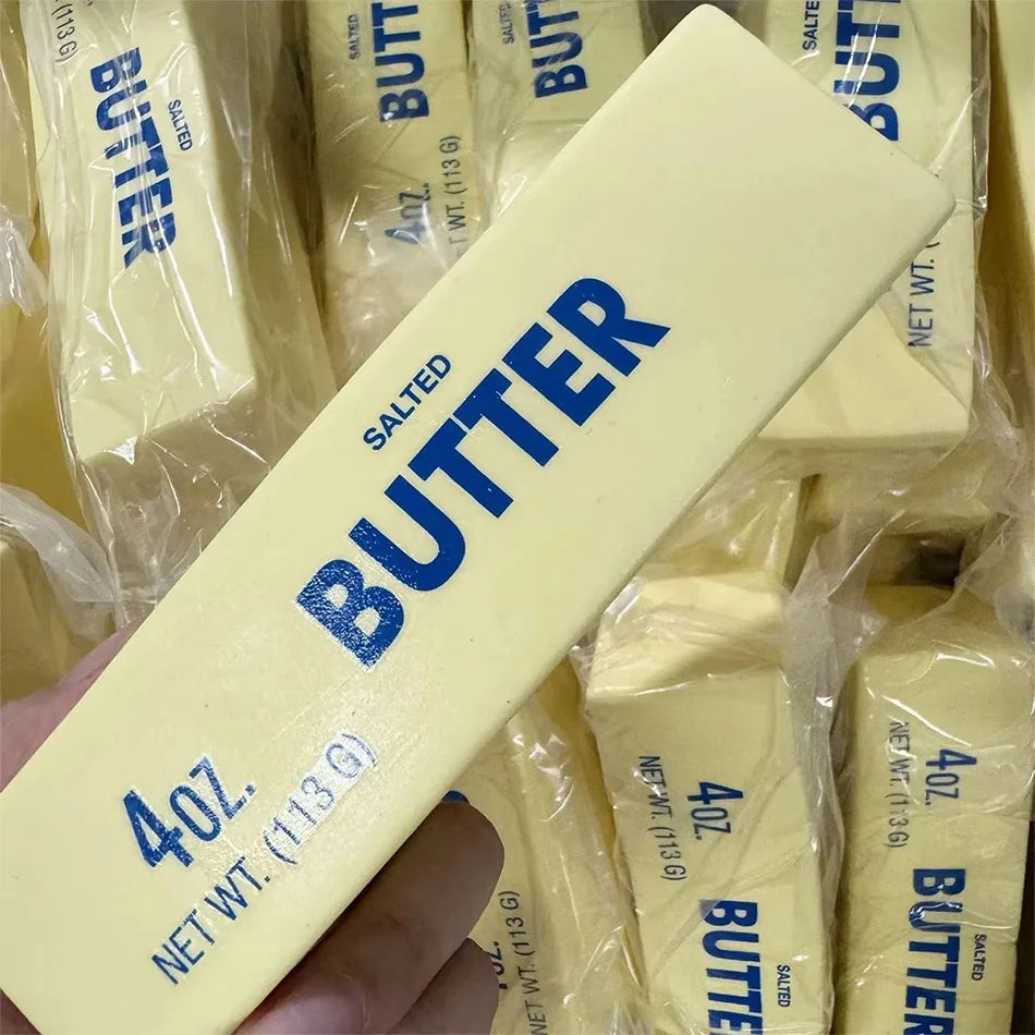 A hand holds a yellow butter squishy stress relief toy packaged in clear plastic bags.