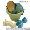 A green plastic bucket contains a beige scoop and a blue shovel, with accompanying sand play accessories.