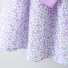 A purple floral dress for a baby girl with white and teal accents and a pink bow detail.