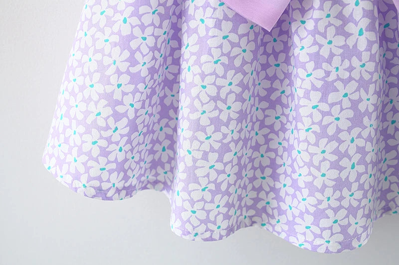 A purple floral dress for a baby girl with white and teal accents and a pink bow detail.